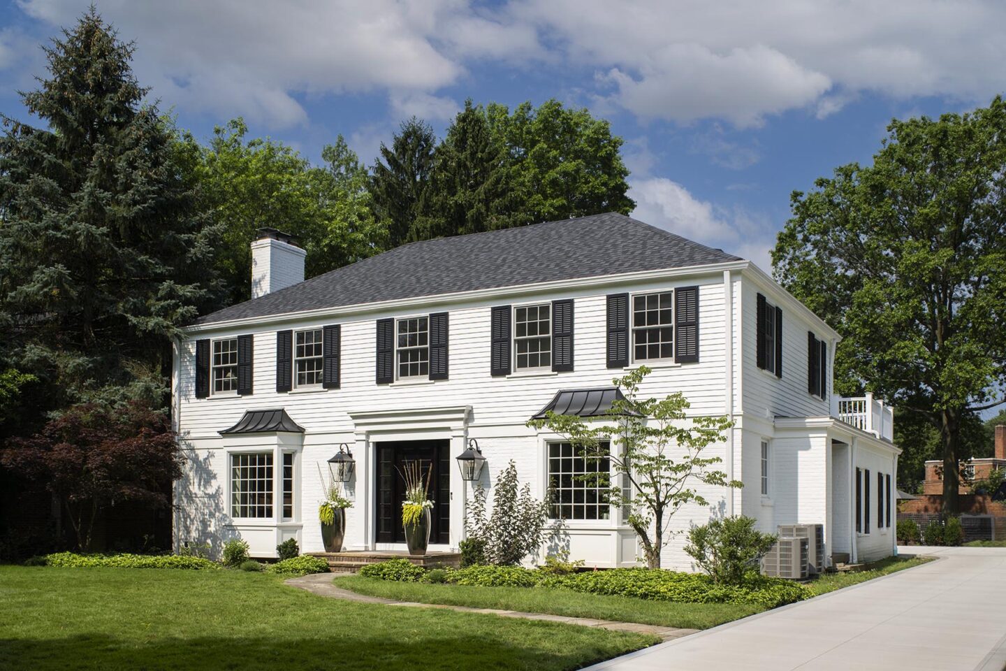 Front view of a beautiful white house with black shutters and doors, manicured landscaping