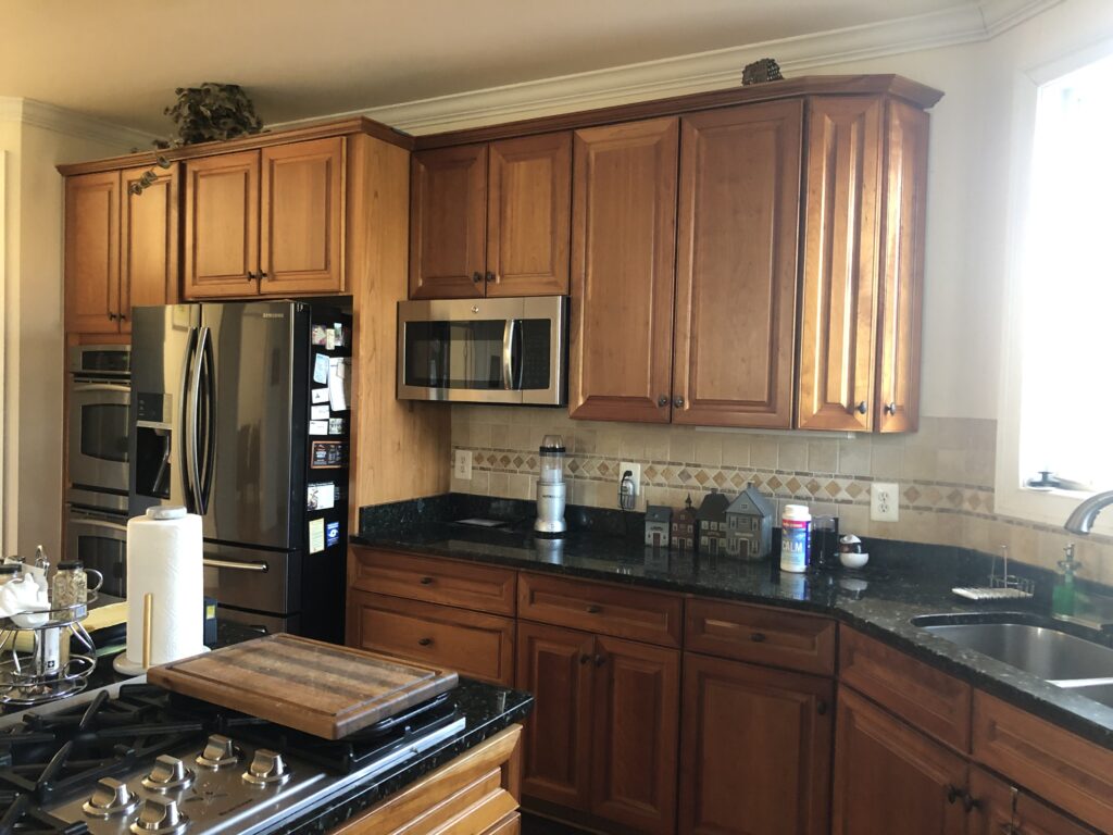 Before remodel – boring builder-grade kitchen in a Purcellville home with standard wood cabinets, dark countertops, and outdated finishes.