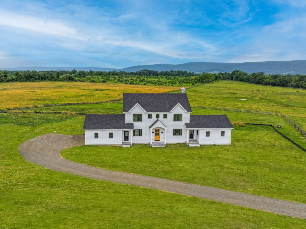 Architectural rendering of a custom two-story white farmhouse with mountain views, circular drive, and expansive countryside lot in Loudoun County.