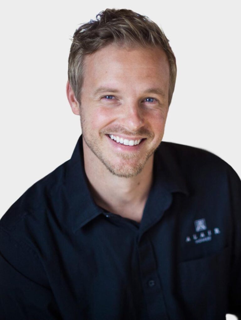 Blair McDaniel, Founder of Alair Homes. Wearing an Alair Homes shirt against pewter background.