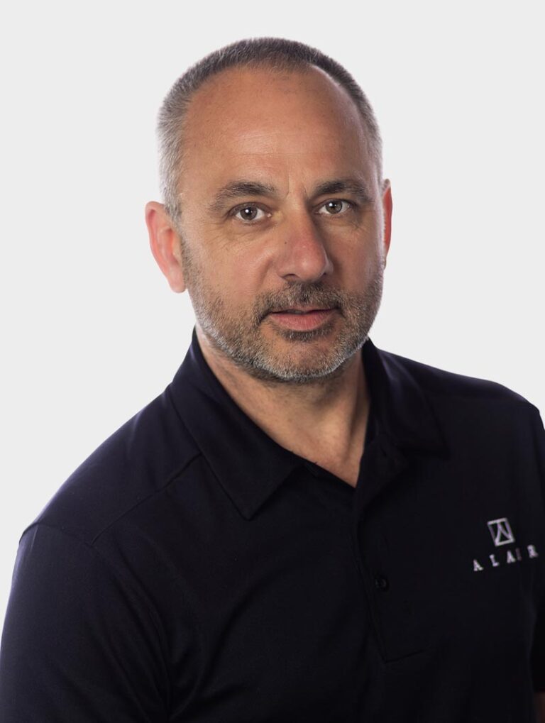 Duane Johns, COO of Alair Homes, Wearing an Alair Homes shirt against pewter background.