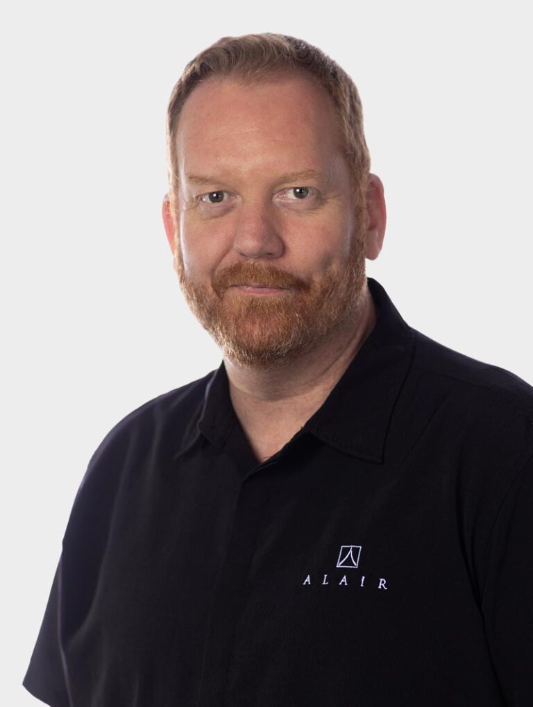 Jeff Daley, Director of Training and Education at Alair Homes, Wearing an Alair Homes shirt against pewter background.
