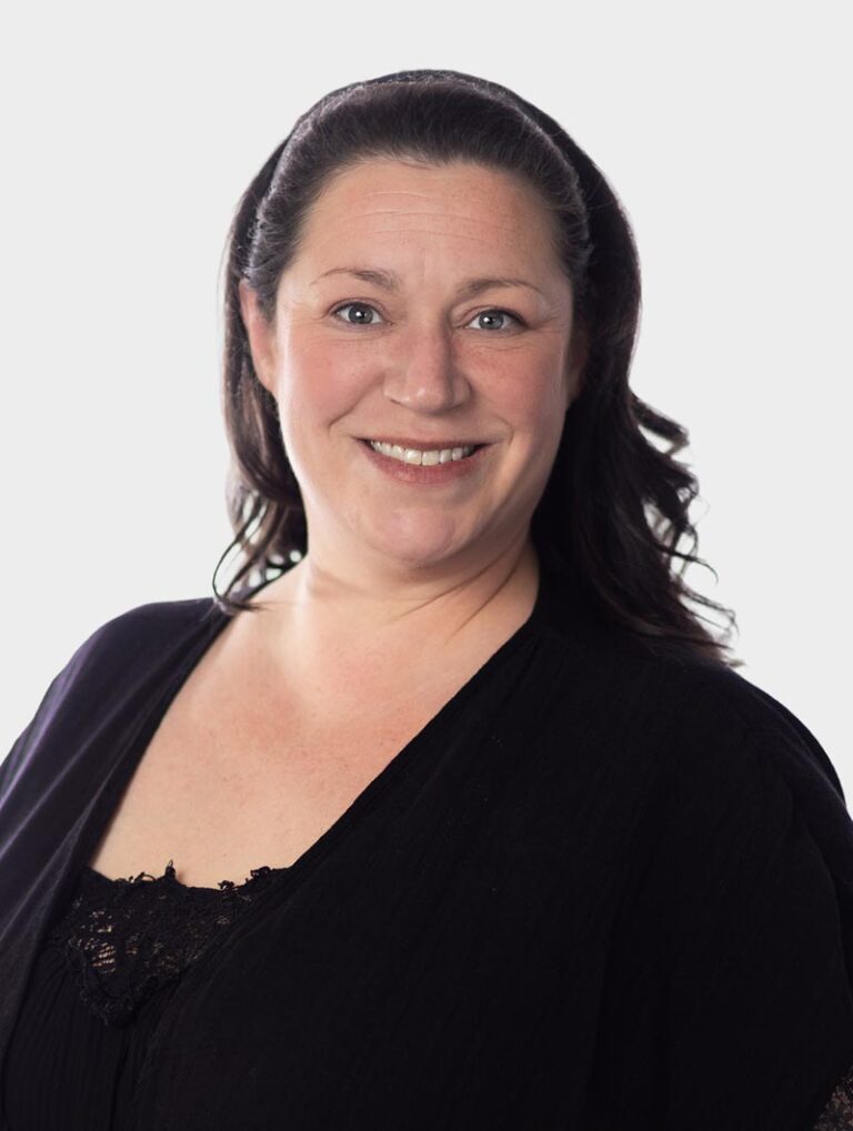 Natalie Harper, Director of Communications, wearing black, posing against pewter background.