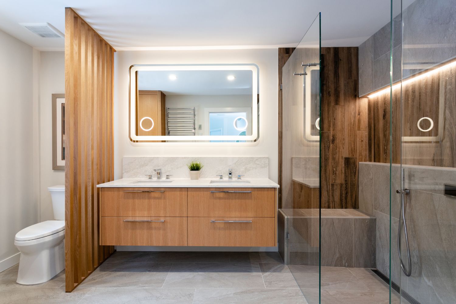 Spa-style bathroom in Vancouver with floating white oak double vanity, quartz countertop, backlit LED mirror, glass shower, and wood-look tile feature wall
