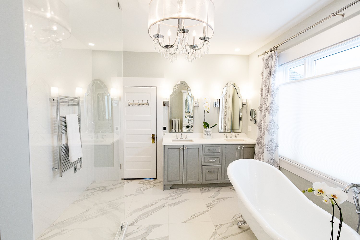 Elegant Richmond ensuite with white clawfoot tub, grey double vanity, arched Venetian mirrors, crystal chandelier, and marble-look tile floors.