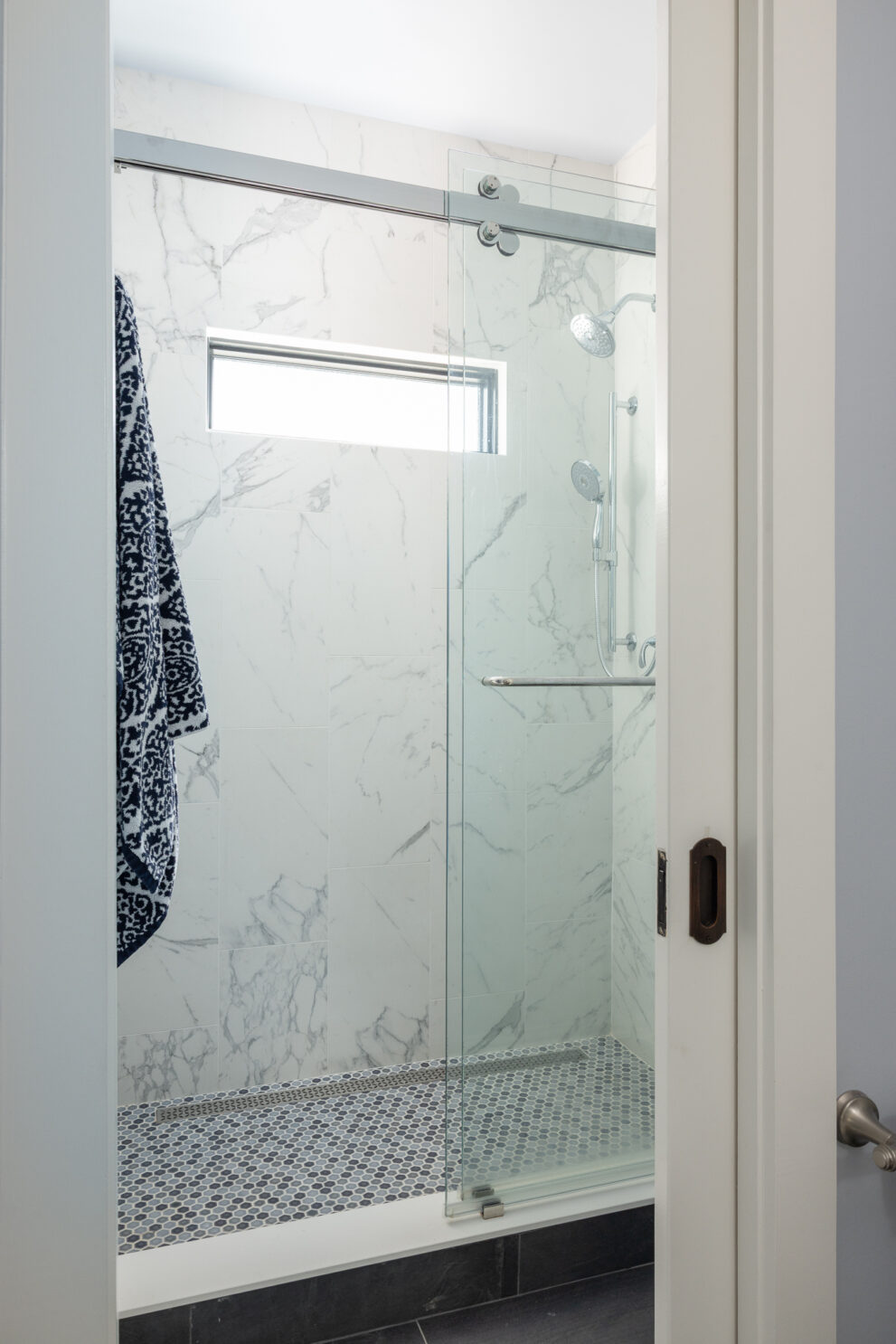 Shower with grey tile hidden behind pocket doors in the first-floor powder room.