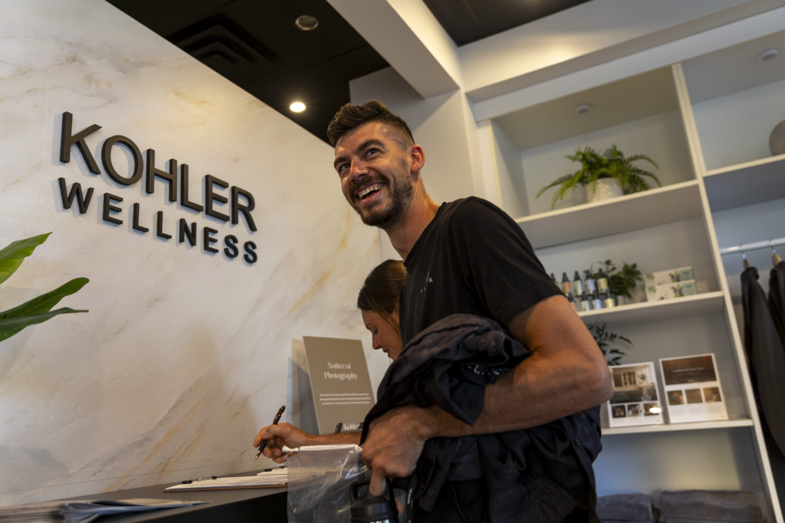 Man in black shirt smiles next to an interior sign that reads 