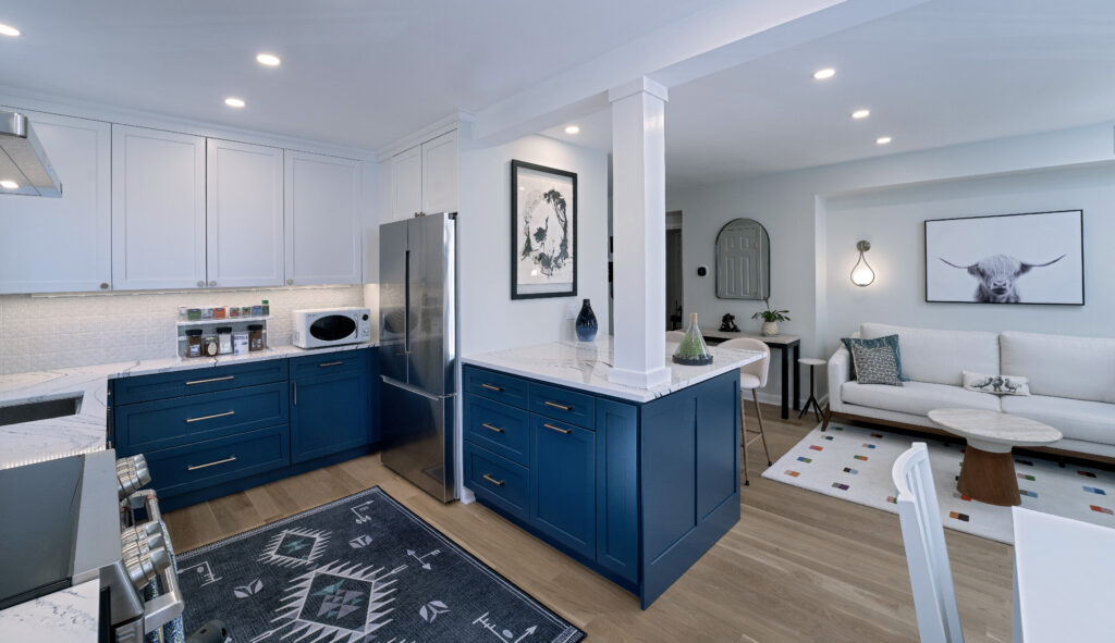 View of a kitchen with white and blue cabinets with an open layout into a living space with a couch.