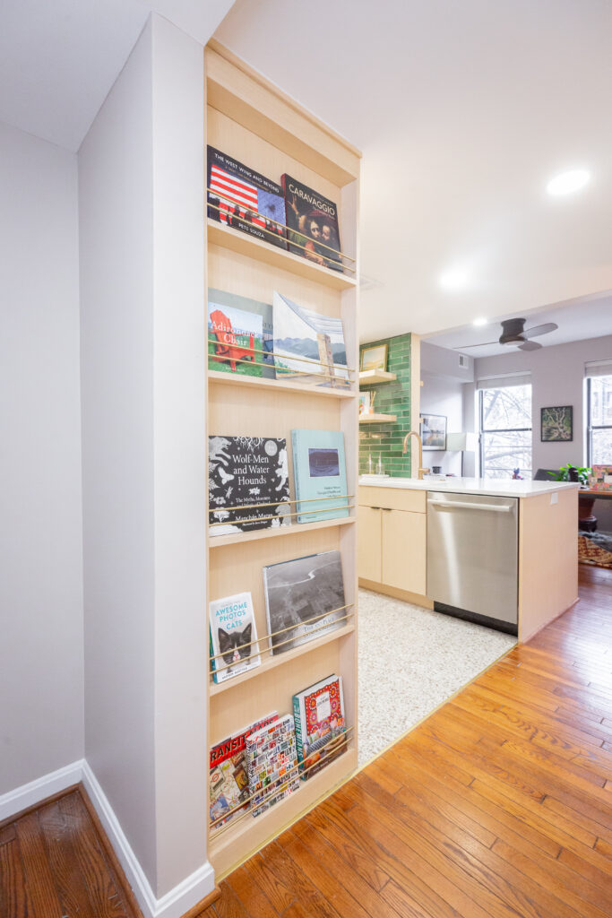 Custom built-in display shelf with champagne brass rods, holding books and magazines, adjacent to the renovated kitchen with green tile backsplash.