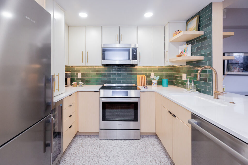 Remodeled kitchen with stainless steel stove and microwave, green subway tile backsplash, white upper cabinets, and open wood shelves.