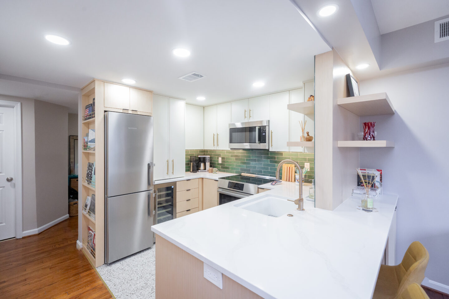 Renovated condo kitchen with white quartz countertops, light wood cabinets, green tile backsplash, stainless steel appliances, and open shelving.