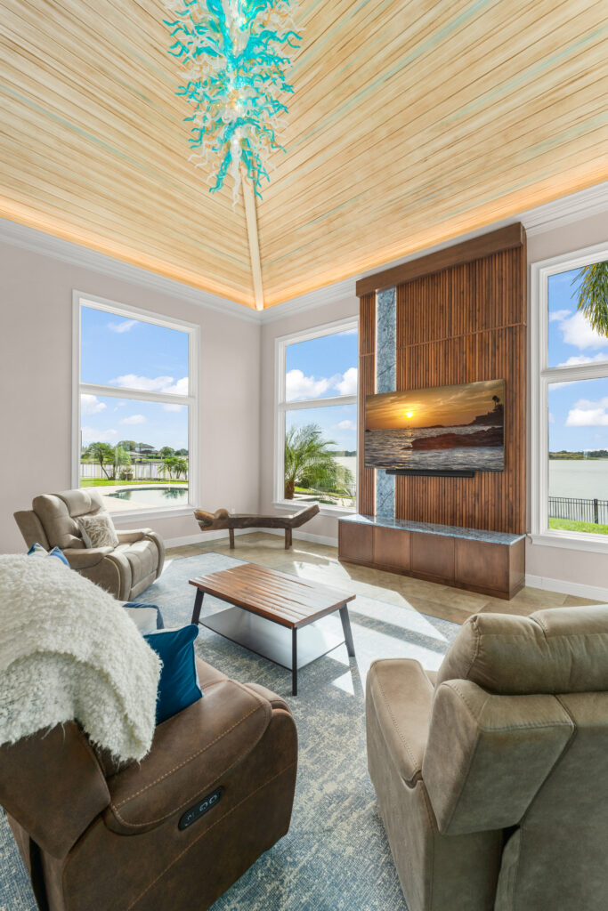 Open-concept living area remodel featuring a large vaulted wood ceiling with decorative lighting, and expansive windows overlooking a waterfront view.