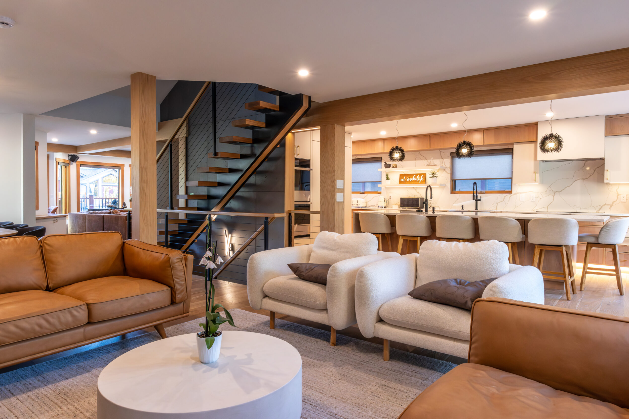 Open-concept Bow Valley home renovation showcasing a warm, mountain-modern living room flowing into a custom kitchen with natural wood beams, modern staircase, and functional layout designed to improve daily living, energy efficiency, and long-term home value in Canmore