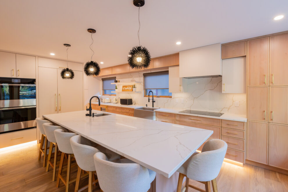 Mountain-modern Bow Valley kitchen renovation in Canmore featuring a large quartz waterfall island, warm wood cabinetry, integrated lighting, and contemporary pendant fixtures designed to enhance everyday functionality, energy efficiency, and long-term home value