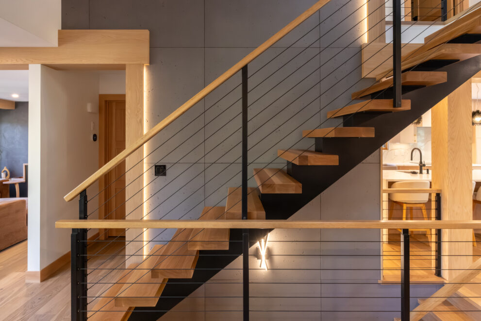Custom mountain-modern staircase in a Bow Valley home renovation featuring floating wood treads, sleek black steel stringer, and cable railing, designed to enhance natural light flow, spatial openness, and long-term architectural value in Canmore.
