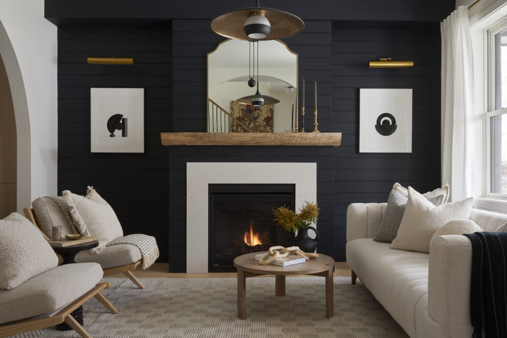 Living room with navy blue wall, white trim, wooden mantels, inset fireplace, and khaki coloured furniture.
