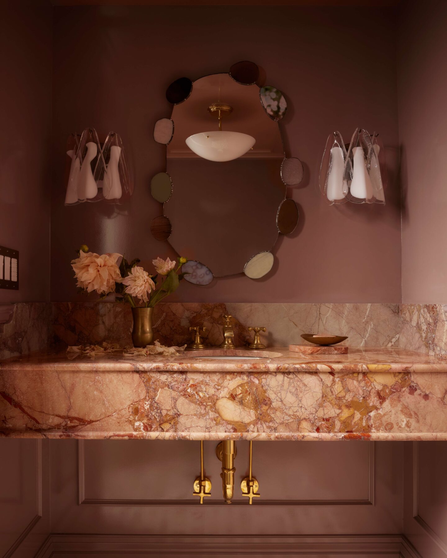 Powder rooms are one of the few places in a home where you can take a design risk: walls wrapped in pink, a richly veined stone that carries the palette through the room, and a stained glass mirror.