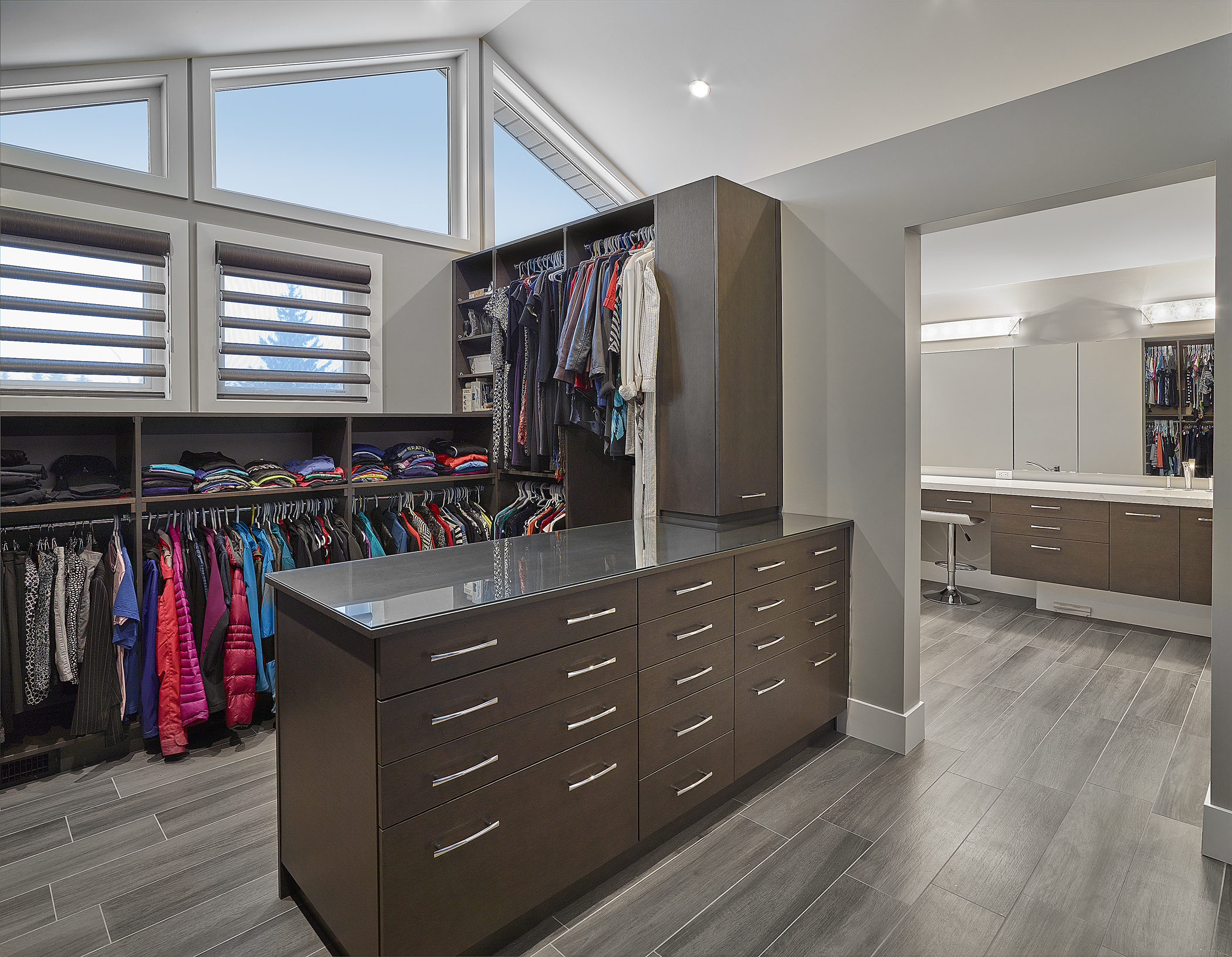 Wheelchair-accessible walk-in closet with hangers low enough for wheelchair height, a dresser with low, wide drawers, and wide clearances between furniture for wheelchair accessibility.
