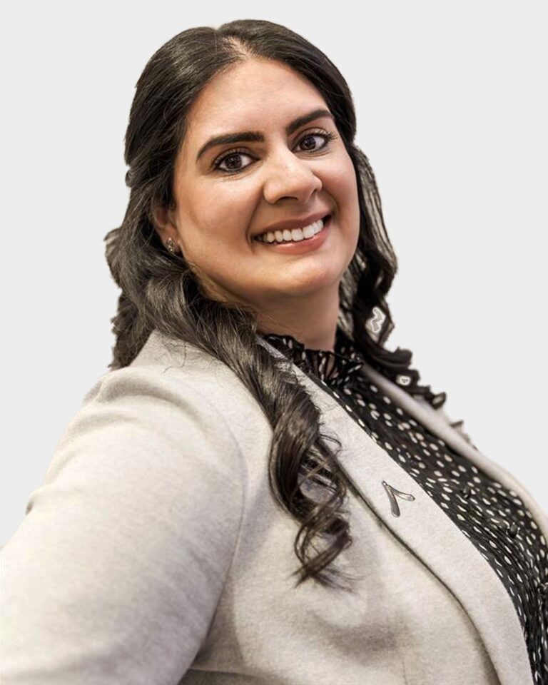 3/4 smiling profile headshot of Mandeep Randhawa, wearing white blazer with Alair logo pin on lapel