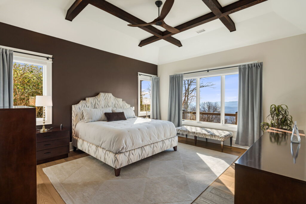 Bright custom bedroom with wood beam ceiling, large windows, and mountain views