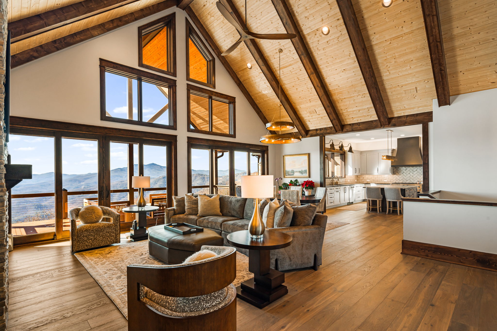Open concept living room with wood beam ceiling, large windows and mountain views, connected to kitchen and dining area Provide your feedback on BizChat