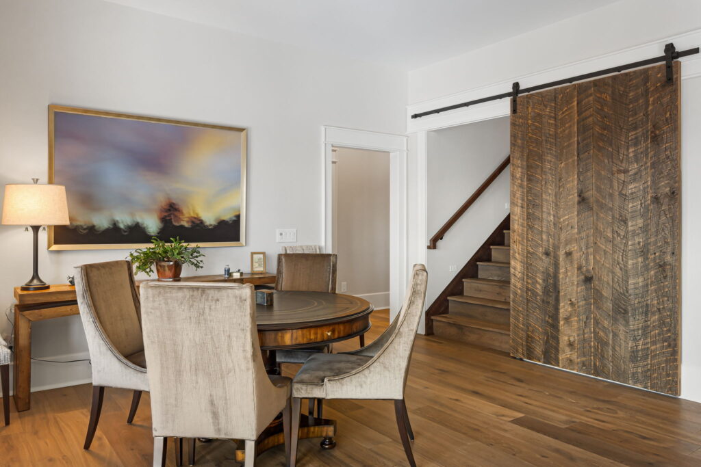Dining area with round table, upholstered chairs and sliding barn door near staircase with wood floors