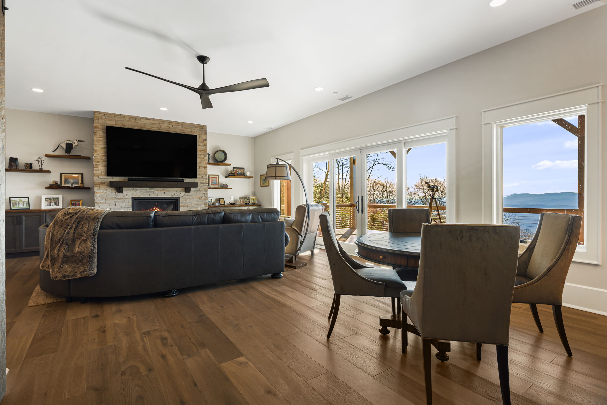 Open living room with stone fireplace, large windows, mountain views and dining area with wood floors