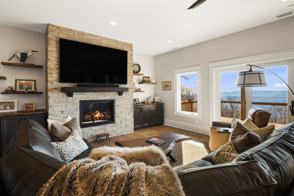 Cozy living room with stone fireplace, large TV, leather seating and mountain views through sliding glass doors