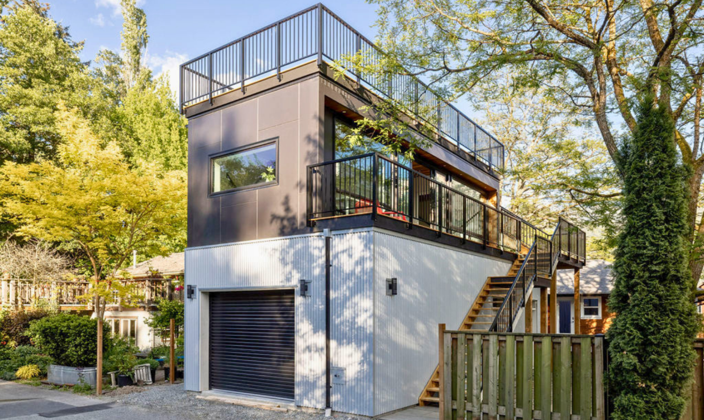 3/4 angle of a 2-storey carriage house, with a roof framed by steel black railing.