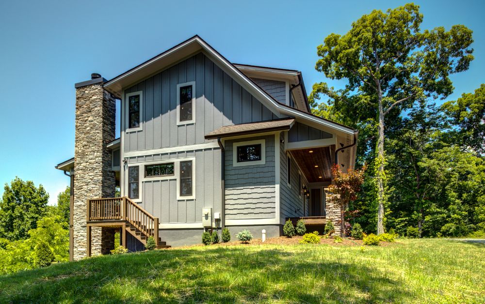 Custom modern mountain home with gray siding, stone chimney, and wooded High Country setting.