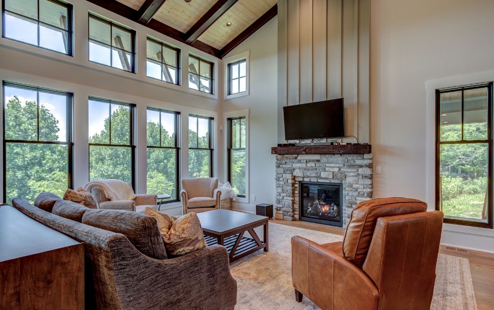 Living room with vaulted ceilings, stone fireplace, and large windows overlooking the surrounding landscape.