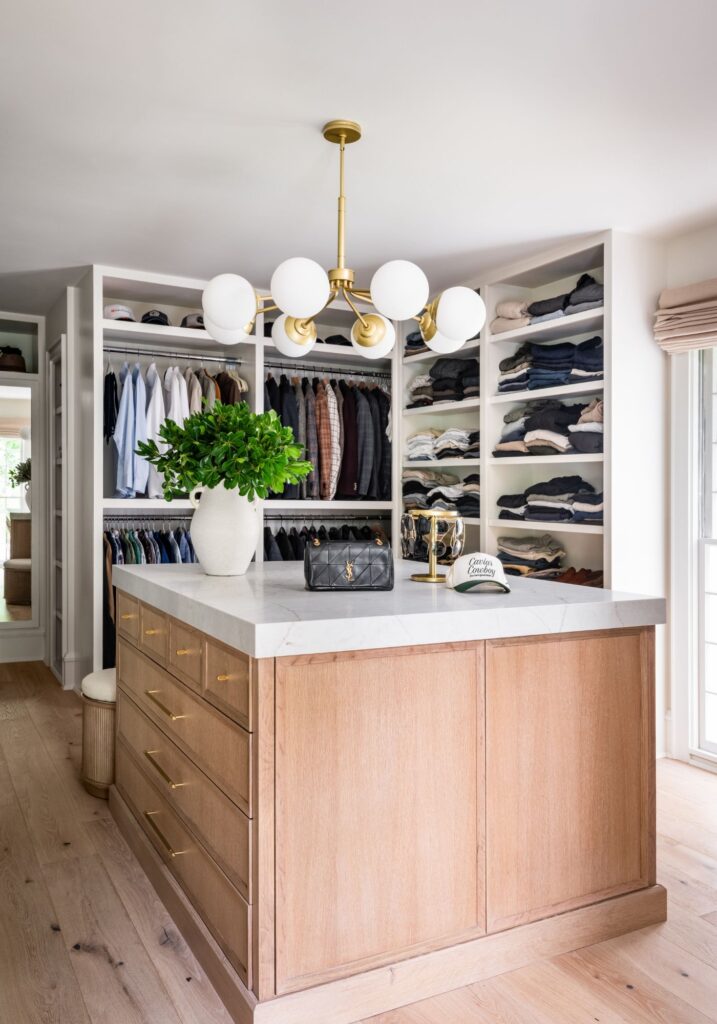 Spacious walk-in closet featuring a marble-topped storage island, custom wood cabinetry, open shelving, and organized wardrobe storage.
