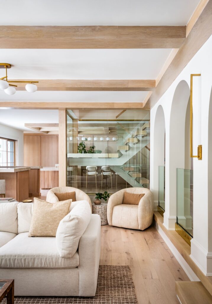Living area with white oak ceiling beams, arched openings, glass railings, and a glass-enclosed staircase that creates a striking architectural focal point.