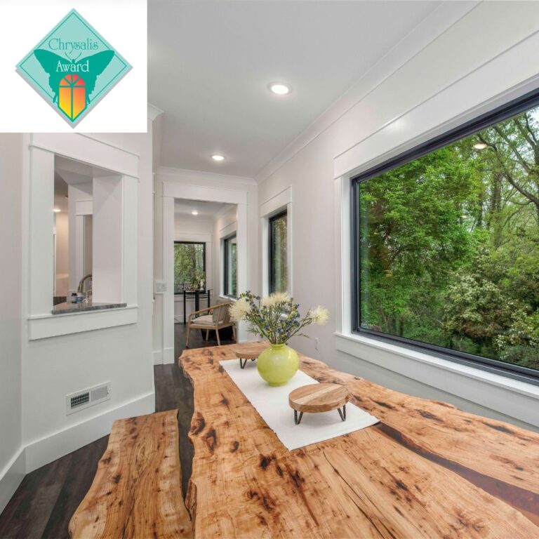 Award-winning whole-home remodel by Alair Hickory featuring a live-edge wood dining table, expansive picture windows, modern trim details, and views of the surrounding landscape.
