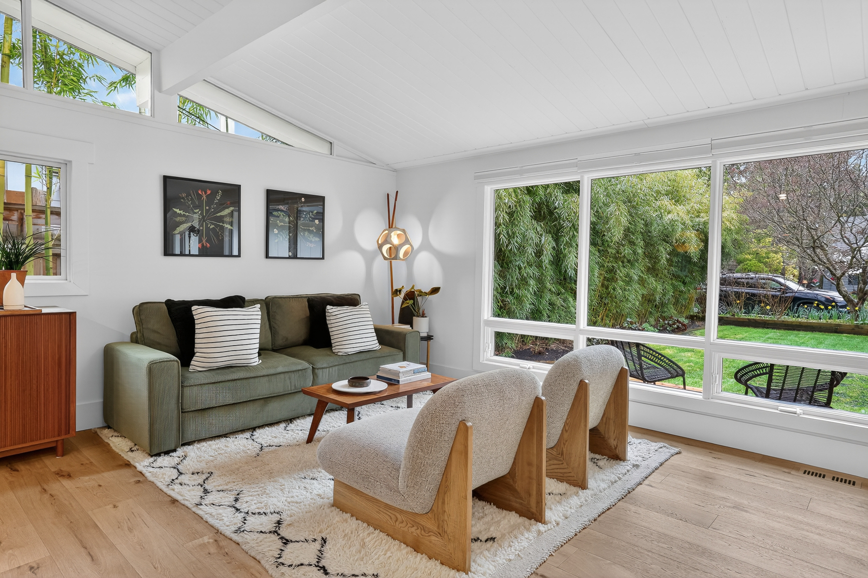 right mid-century living room with vaulted ceiling, clerestory windows, white oak floors, and large picture windows overlooking the garden.